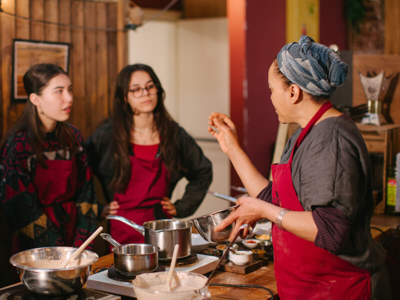 Two women are watching a cooking teacher demonstrate how to make Ethiopian food